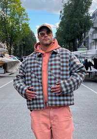 Giacca a quadri marrone e azzurro chiaro con una vestibilità ampia, chiusura con zip e grandi tasche, indossata sopra un hoodie pesca e pantaloni abbinati.