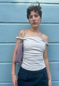 Αμάνικο ανοιχτό γκρι τοπ με υφή, συνδυασμένο με ψηλόμεσες μαύρες παντελόνες. Μια μικρή μωβ τσάντα χεριού με διάφανο λουρί.