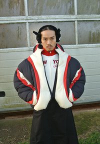 Jachetă pufosă chunky bicoloră în nuanțe de navy și crem, cu accente roșii, pulover texturat alb cu inscripția "NEW YORK" și căști mari de urechi.