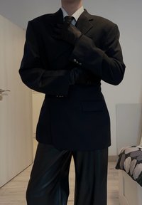 Must toonist lahtine bleiser, millel on lõigatud ja struktuursed õlad, kombineeritud siledatest mustast nahast pükstega. Model kannab musti kindaid, lipsud on nähtaval.