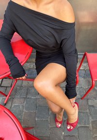 Svart off-shoulder langermet topp parret med et tettsittende svart skjørt. Viser røde åpen tå-sko med dekorative sløyfer, sittende på en rød stol.