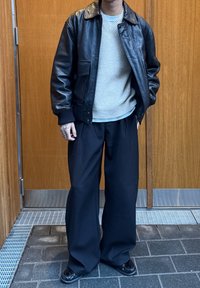 Crna kožna bomber jakna s rebrastim manšetama preko svijetlosivog pletenog džempera i širokih crnih hlača. Tanki crni cipele upotpunjuju izgled.