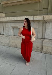 Robe rouge ajustée avec un détail noué à la taille, associée à des sandales blanches et un sac léger. Matière lisse, design sans manches.