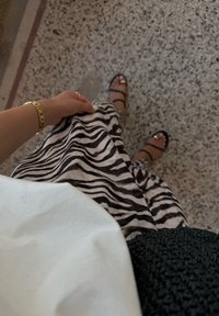 Saia com padrão de zebra em preto e branco, feita de tecido leve, combinada com sandálias pretas de tiras. Mão segurando a bainha da saia visível.
