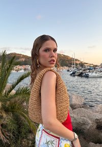 Woven straw shoulder bag in a rounded, structured shape, featuring a natural beige color and textured surface, with a smooth strap.