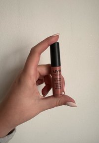 NYX Soft Matte Lip Cream in a cylindrical tube, featuring a black cap and pinkish-brown liquid. Text labels in black, size 0.27 fl oz.