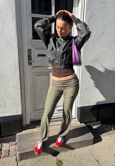 Chaqueta de cuero negra corta, blusas en capas marrones, pantalones de campana verdes oliva y zapatillas rojas con rayas blancas. Acento de bolso morado.