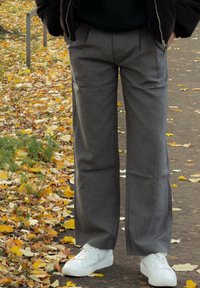 Szürke csíkos, kényelmes szabású nadrág, fehér sportcipővel párosítva, háttérben őszi falevelekkel egy ösvényen.