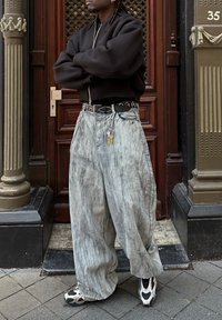Laza szürke farmernadrág textúrával, fekete cipzáras bomber dzsekivel párosítva. Kiegészítők között van egy szegecses öv és kulcsok.