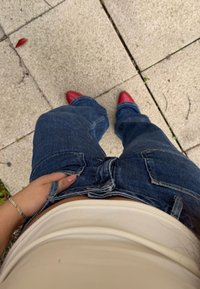 Modré džíny z denimu s velkými kapsami a uvolněným střihem, v kombinaci s červenými špičatými botami. Pas je držení jednou rukou.