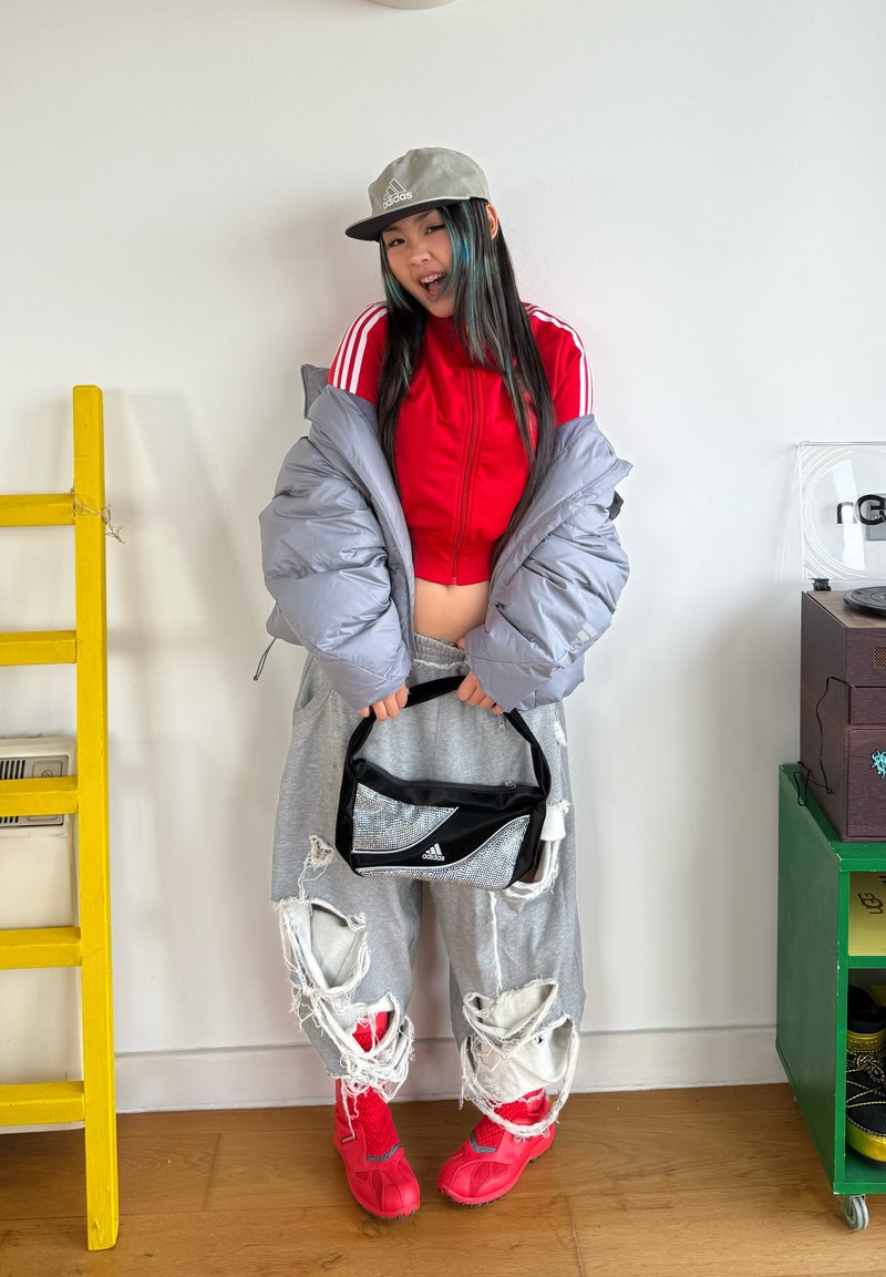 Grey distressed joggers with large rips, red cropped jacket, oversized grey puffer jacket, black bag, and bright red footwear.