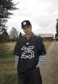 Czarny t-shirt z białą grafiką "25", krótkie rękawy z fioletowymi akcentami, noszony na paskowanym długim rękawie, w połączeniu z ciemnymi dżinsami i czapką w kolorze czarnym.