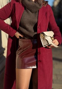 Βουργουνδιά-wool παλτό με μεγάλα κουμπιά, καφέ ριγωτό τσάκετ, γυαλιστερή βουργουνδιά μίνι φούστα και λευκή τσάντα με χρυσές λεπτομέρειες.