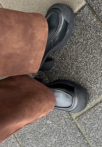 Scarpe con platform nere, con punta arrotondata e suola in gomma spessa. Dettaglio di cucitura a contrasto, indossate con un indumento in suede marrone.