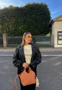 Zwarte leren bomberjack, witte langesleeve shirt, zwarte rok en een geweven oranje tas met een zachte charm eraan bevestigd.