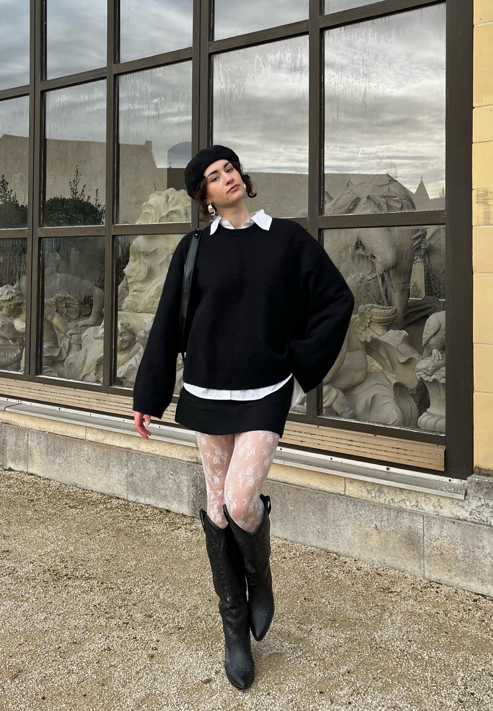 Svart oversized tröja, vit skjorta under, svart minikjol, vita blommönstrade strumpbyxor och knähöga svarta stövlar.