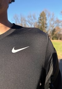 Camiseta deportiva negra hecha de tela transpirable, con cuello redondo y un logo blanco de Nike en el lado izquierdo del pecho.