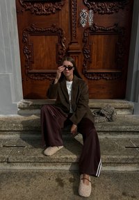 Brun cordfløyelsblazer, hvit skjorte, brune vide bukser med hvite striper. Beige, pusete slip-ons. Leopardmønstret veske ved siden av personen på steintrappen.