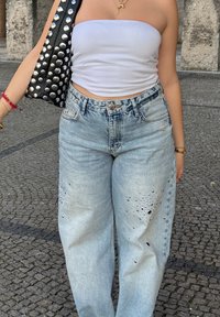 Jeans in denim blu chiaro strappati con una vestibilità ampia, caratterizzati da un'alta vita e dettagli sfrangiati, abbinati a una borsa nera con borchie sulle spalle.