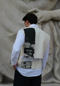 Bežna brezrokavnik z black barvami, kot so poteze na hrbtni strani, nošena čez belo srajco, prikazana na teksturirani kamniti podlagi.