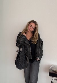 Veste de motard en cuir noir avec garnitures argentées, portée sur un haut noir à détails en dentelle. Associée à un jean gris foncé et un sac noir décontracté.