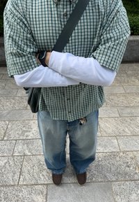 Grön och vit rutad kortärmad skjorta över en vit långärmad skjorta, matchad med lösa blå jeans och bruna skor. Nyckelring synlig.