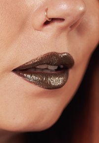 Metallisch donkerbruine lippenstift met een glanzende afwerking, aangebracht op volle lippen. Gouden neushaak accent is zichtbaar. Soepele textuur en glans.