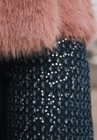 Blană artificială de un roz delicat peste un material întunecat cu paiete, prezentând o suprafață texturată cu paiete lucioase și reflectorizante aranjate într-un model.