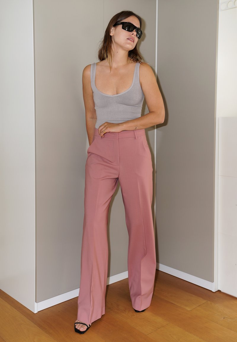 Harmaa ribbattu toppi, joka on yhdistetty korkeavyötäröisiin, vaaleanpunaisiin leveälahkeisiin housuihin. Mustat neliönmalliset aurinkolasit ja mustat korotut sandaalit täydentävät asua.