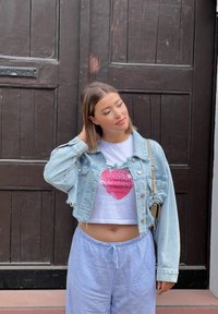 Gai zila denima īsā jakā ar priekšējām kabatām virs baltas T-krekla ar rozā zemeņu apdruku, kombinācijā ar gaiši zilām svītrainām biksēm.