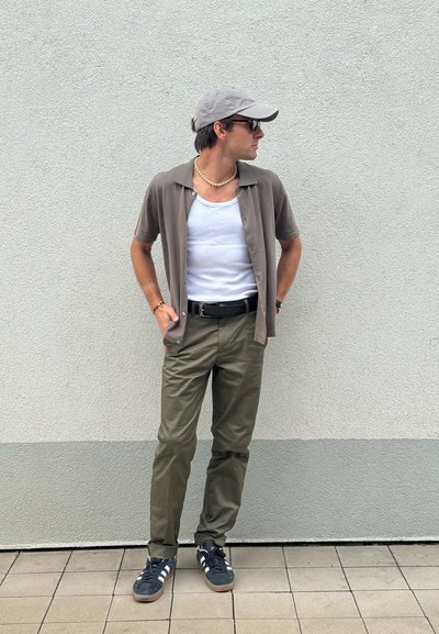 Camisa de botones de manga corta, color marrón claro, sobre un top blanco; pantalones verdes oliva; gorra gris; cinturón negro; deportivas oscuras con rayas blancas.