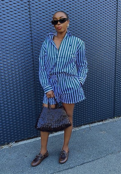 Vestido de camisa a rayas azul y verde con pantalones cortos a juego, combinado con un bolso tejido negro y mocasines marrones.