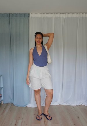 Body de cuello halter azul marino, pantalones cortos plisados color beige claro y chanclas oscuras. Texturas suaves, colores contrastantes y diseño casual.