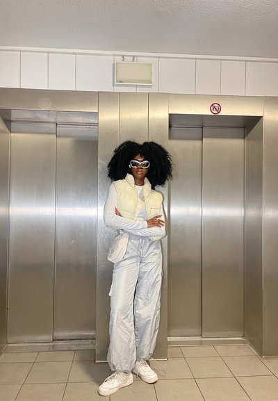 Chaleco acolchado blanco sobre una camiseta de manga larga, pantalones cargo gris claro y zapatillas blancas. Accesorios como gafas de sol blancas y un bolso pequeño.