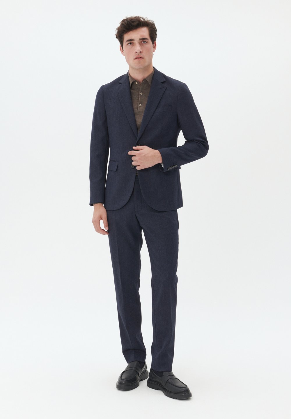 Tumed ülikond, millel on vormitud disain, tekstureeritud kangas, kahe nööbiga bleiser ja lamedate otsadega püksid, koos pruuni kraega särk ja mustade jalanikega.