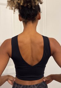 Czarny sportowy top typu crop z głębokim dekoltem w kształcie litery V z tyłu, dopasowany, gładki w dotyku, bez widocznych elementów metalowych ani wzorów.