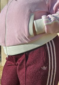 Veste zippée rose côtelée avec poignets rayés blancs, associée à un pantalon de jogging bordeaux duveteux avec trois bandes blanches et un logo Adidas.