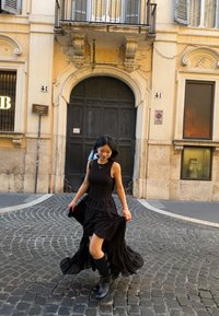 Μαύρο φόρεμα μήκους έως το γόνατο με εφαρμοστό πάνω μέρος και αέρινη φούστα· συνδυασμένο με μαύρες μπότες μέχρι το γόνατο. Κοτρόνες δρόμου στο φόντο.