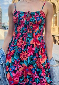 Λουλουδάτο φόρεμα με ντεκολτέ που διαθέτει ζωντανό μοτίβο ροζ, κόκκινων και μπλε λουλουδιών σε μαύρο φόντο, με λεπτές τιράντες και εφαρμοστό κορσέ.