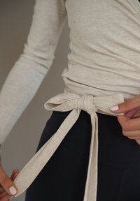 Lichtbeige geribd wikkeltop met een gestrikte accenten, gecombineerd met donkere legging. Focus op textuur en stofdetails.