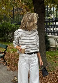 Stripet, lys grå genser med henley-krage, paret med hvite vide bukser. Holder en takeaway-kaffekopp og en liten svart håndveske.