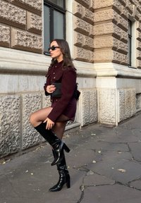 Burgunderfarbene Wolljacke mit goldenen Knöpfen, braunem Mini-Kleid, transparenten Strumpfhosen und knielangen schwarzen Lederstiefeln mit spitzem Schuh und blockiertem Absatz.