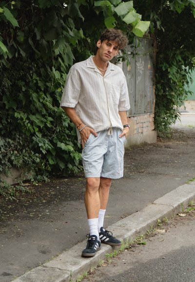 Camisa de botones de manga corta blanca con rayas finas, combinada con pantalones cortos azul claro. Zapatillas negras con rayas blancas y calcetines blancos de caña corta.