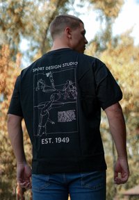 Schwarzes Baumwoll-T-Shirt mit einem grafischen Druck von Basketballspielern, Text "SPORT DESIGN STUDIO" und "EST. 1949" in Weiß. Kurze Ärmel, lässige Passform.