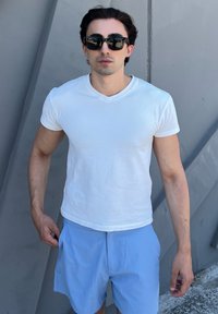Camiseta branca de algodão com decote em V combinada com calções azul claro. Os calções têm bolsos laterais e um corte descontraído. O fundo é cinza.