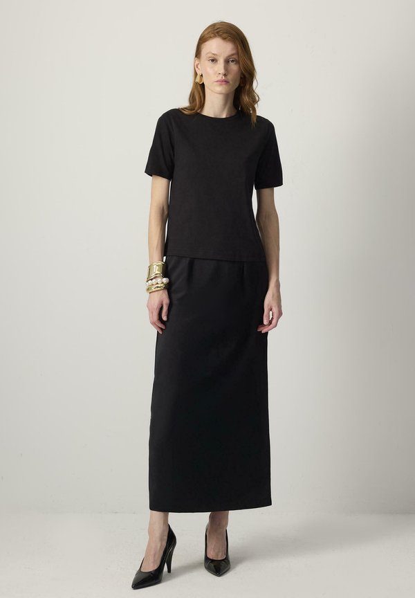 Sort kortærmet top sammen med en lang sort nederdel med en glat tekstur. Med tilbehør i form af guldarmbånd og sorte hæle.