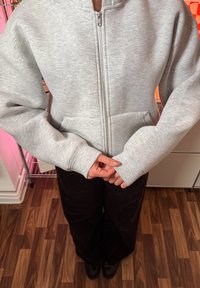 Svetlosivá mikina na zips s textúrovaným povrchom, voľným oversized strihom a prednými vreckami. Dlhé rukávy s rebrovanými manžetami. Kombinovaná s tmavými nohavicami.