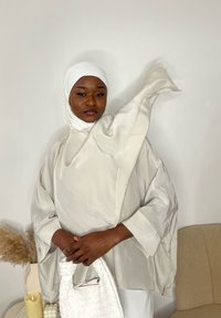 Top gri deschis, mătăsos, cu mâneci supradimensionate și guler înalt. Modelul ține o geantă albă texturată. Baticul alb completează ținuta.