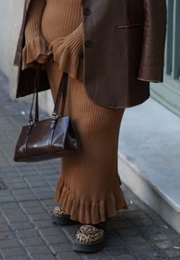 Άτομο που φοράει καφέ ριμπ φούστα με βολάν στο τελείωμα, σκούρο καφέ δερμάτινο μπουφάν, παπούτσια με λεοπάρ σχέδιο, κρατώντας σκούρα καφέ δερμάτινη τσάντα.