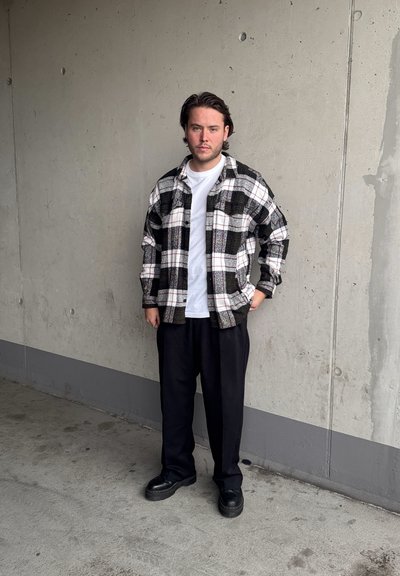 Camisa de franela a cuadros en negro, blanco y gris, superpuesta sobre una camiseta blanca, combinada con pantalones holgados negros y zapatos de plataforma negros.